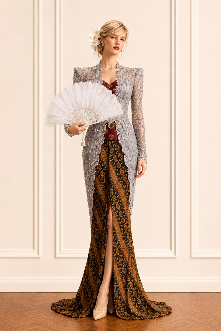 Silver-gray embroidered kebaya layered over a burgundy inner panel and warm brown batik, styled with a white fan.